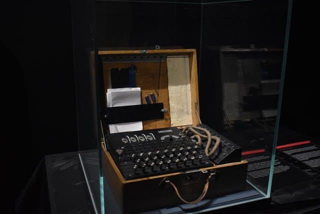 Enigma machine with open case and visible rotors in a museum display.