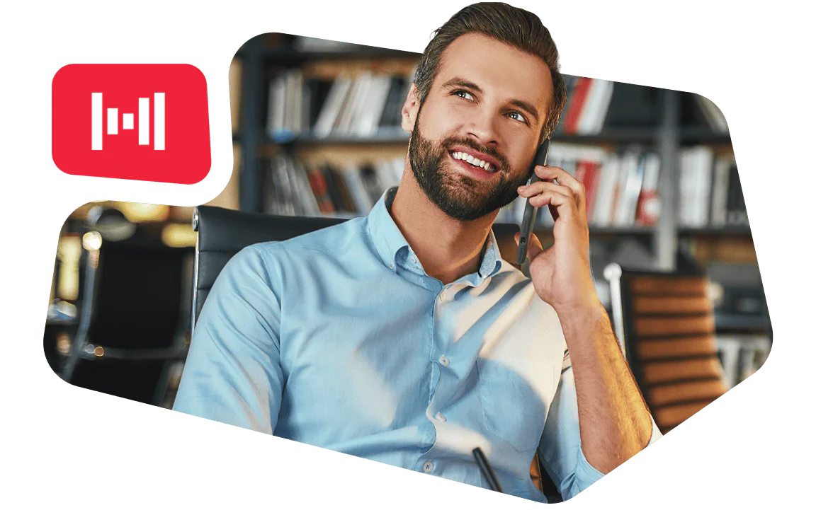 Man smiling and talking on a phone in an office setting with bookshelves in the background.