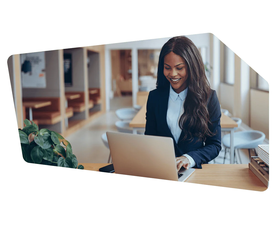 Smiling woman in a business suit using a laptop at a desk in a modern office setting.