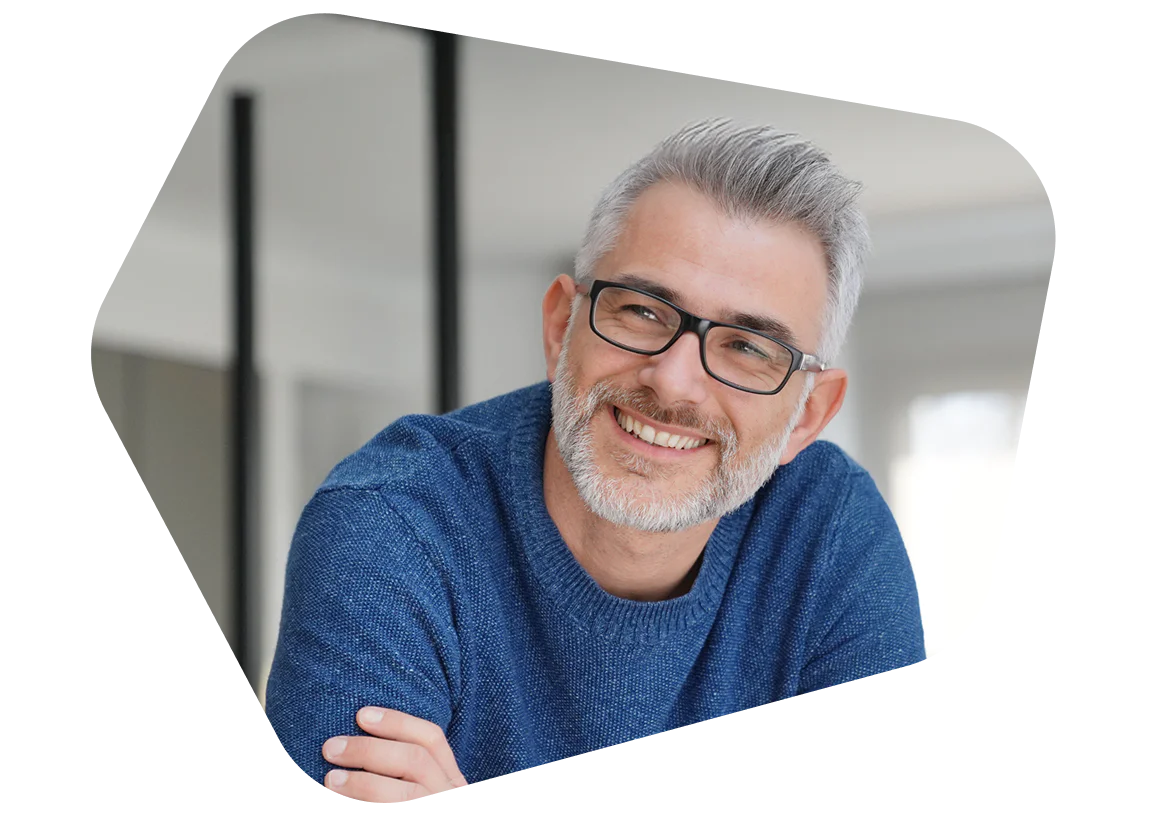 Man with grey hair and glasses wearing a blue sweater smiling indoors