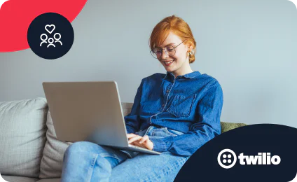 Woman wearing denim, smiling, working on a laptop while seated on a couch.