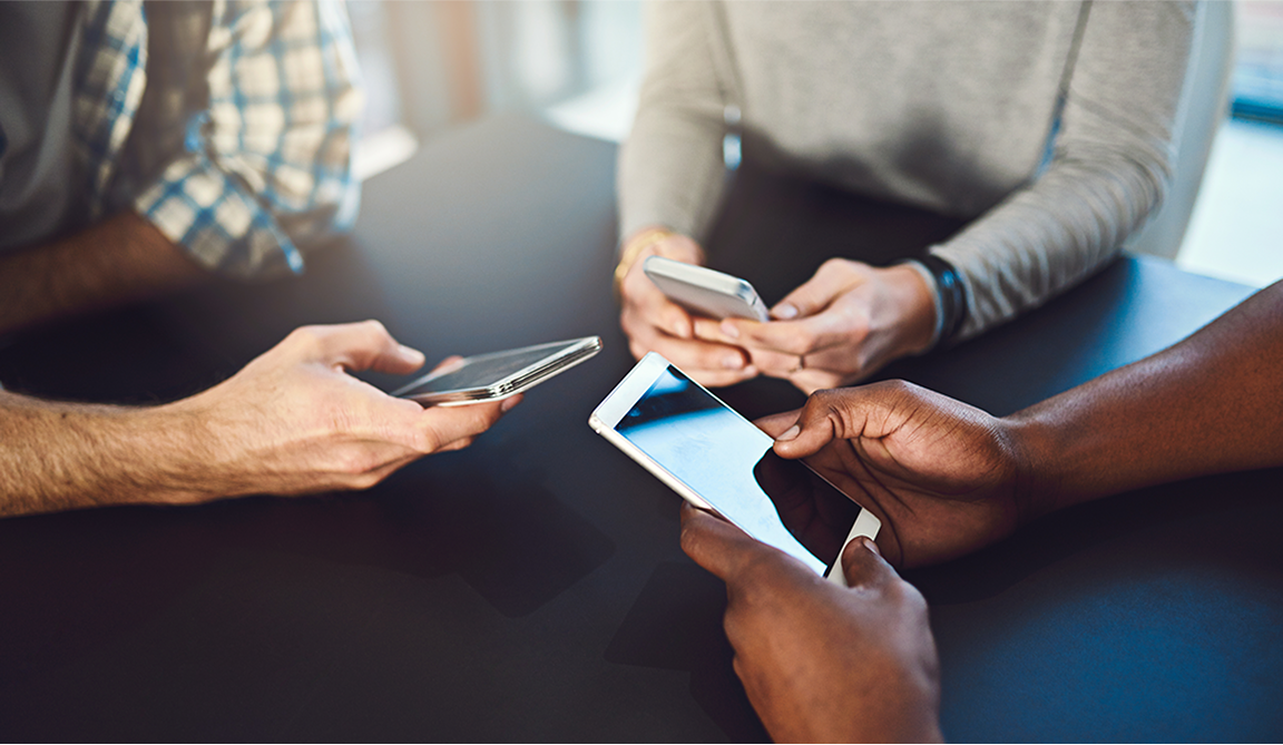 Three people sitting at a table, each holding and using a smartphone.
