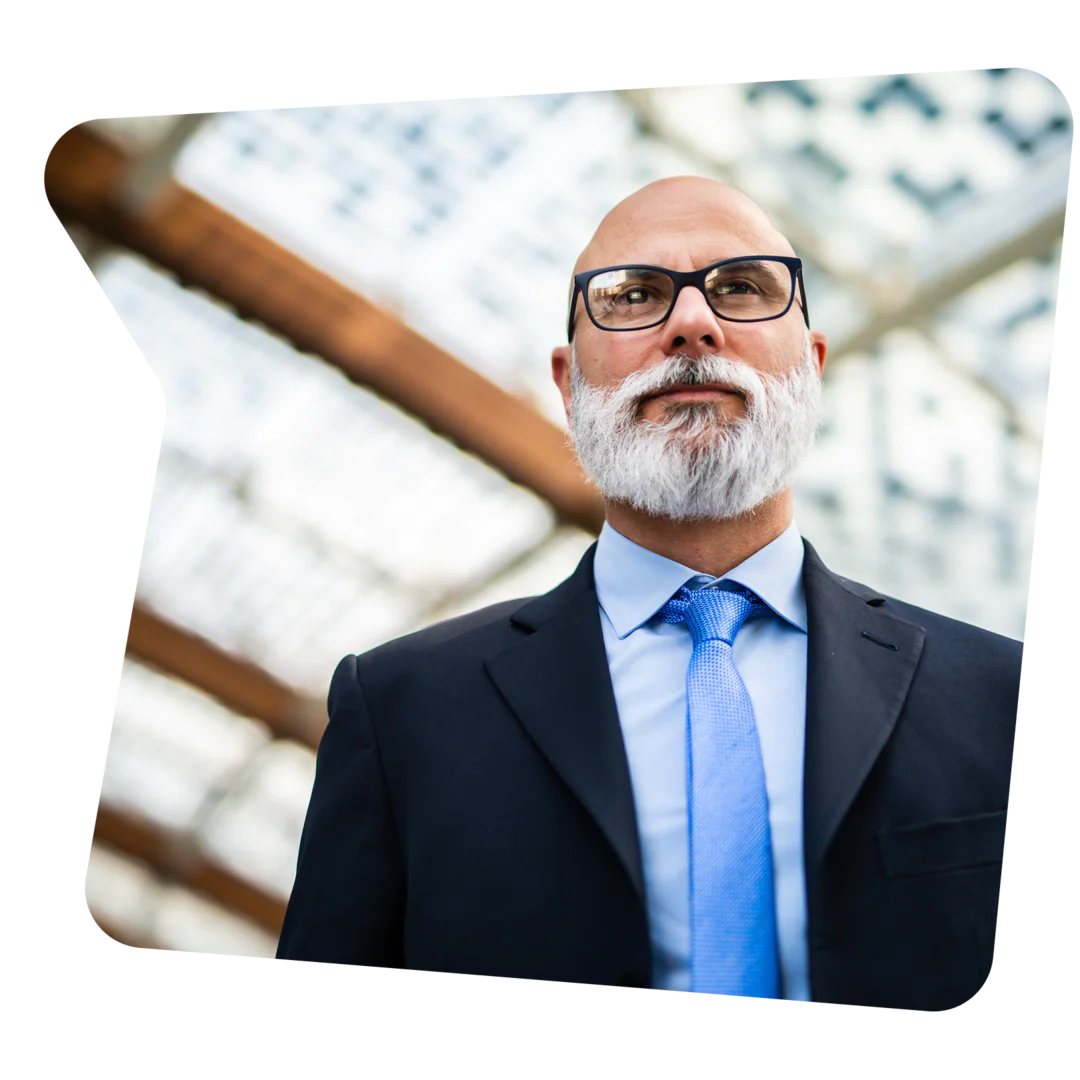 Bald man with a white beard wearing glasses and a suit with a blue tie.