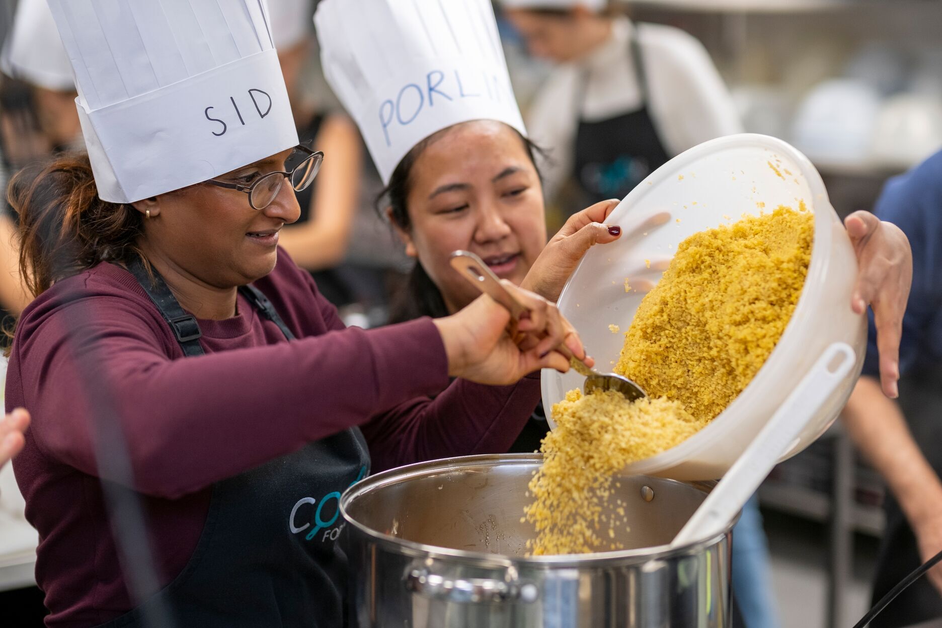 Two people adding ingredients to a pot during a cooking class.