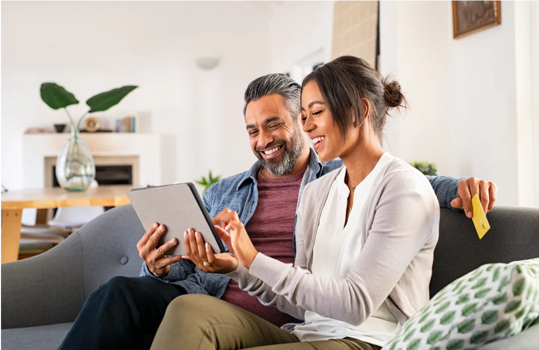 Smiling couple sitting on the couch with a tablet and credit card.