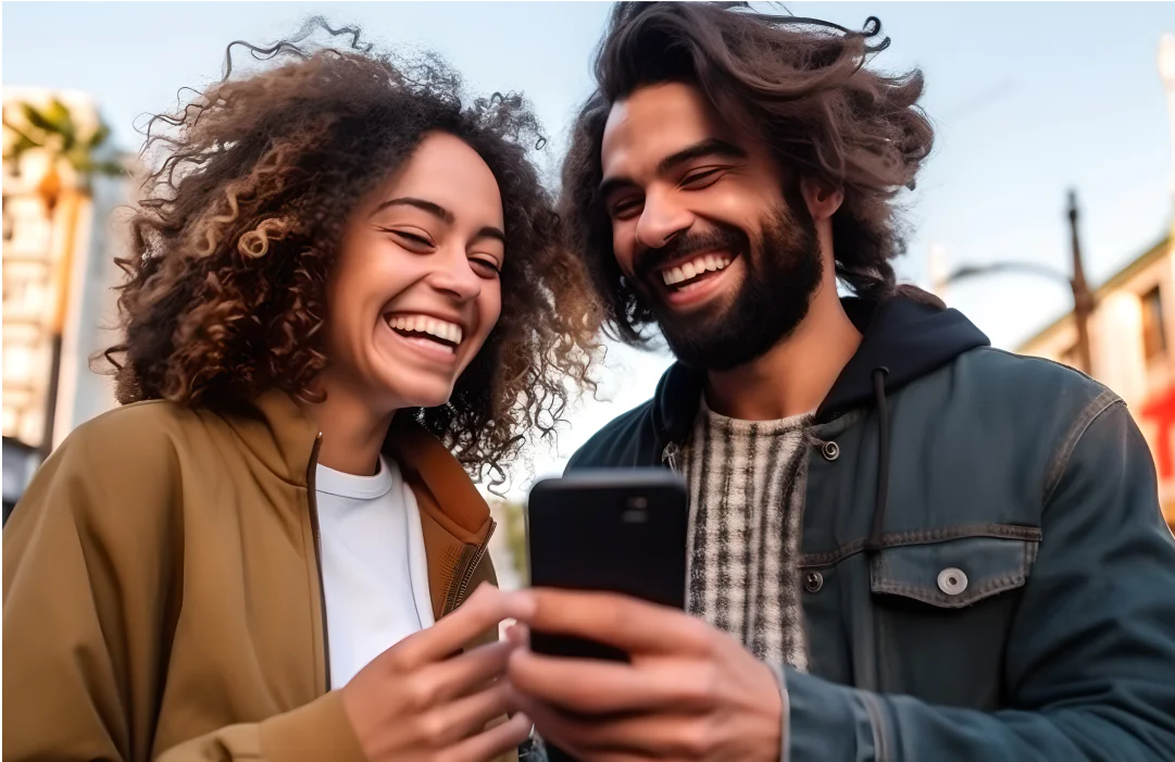 Two friends laughing and looking at a smartphone outdoors.