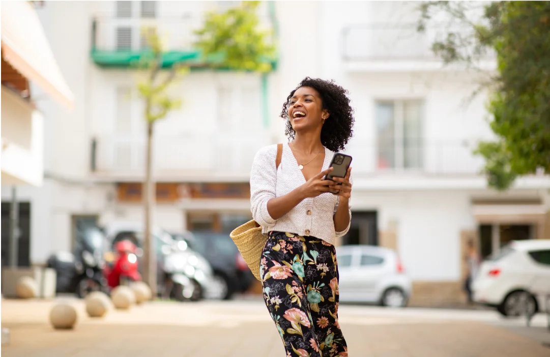 Smiling woman holding her phone and walking outside with a purse