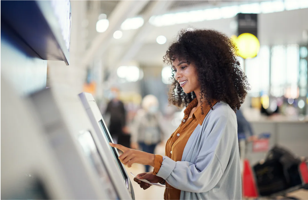 Smiling woman with curly hair uses a self-service kiosk in an airport.