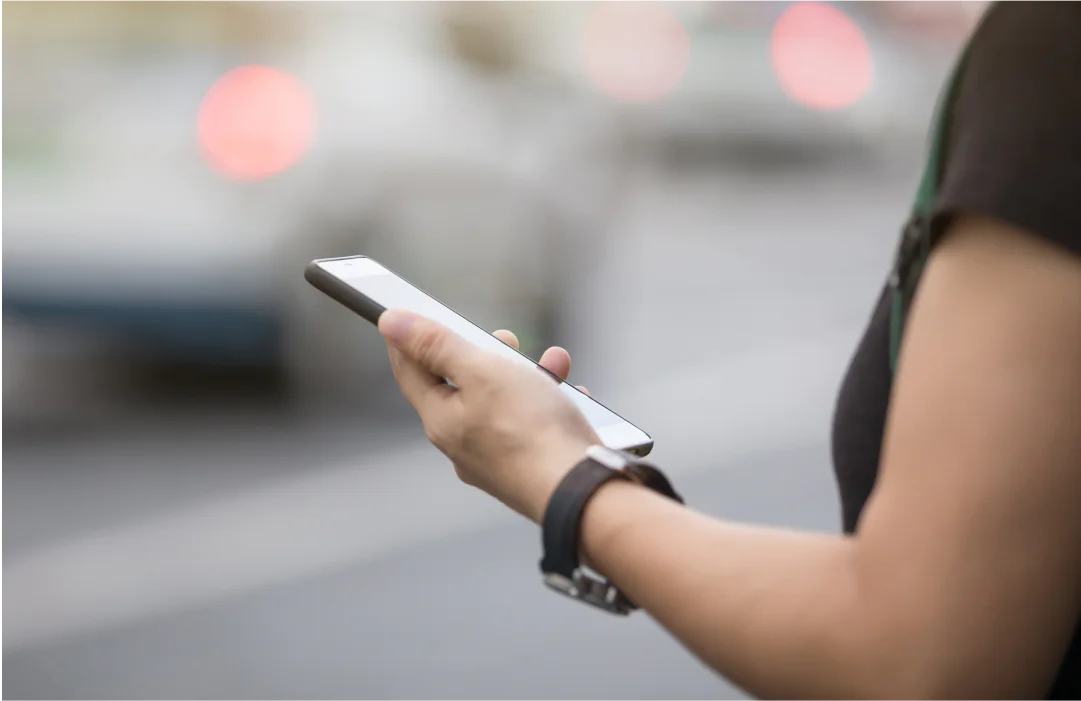 Person holding a smartphone while standing on a busy street with blurred background.