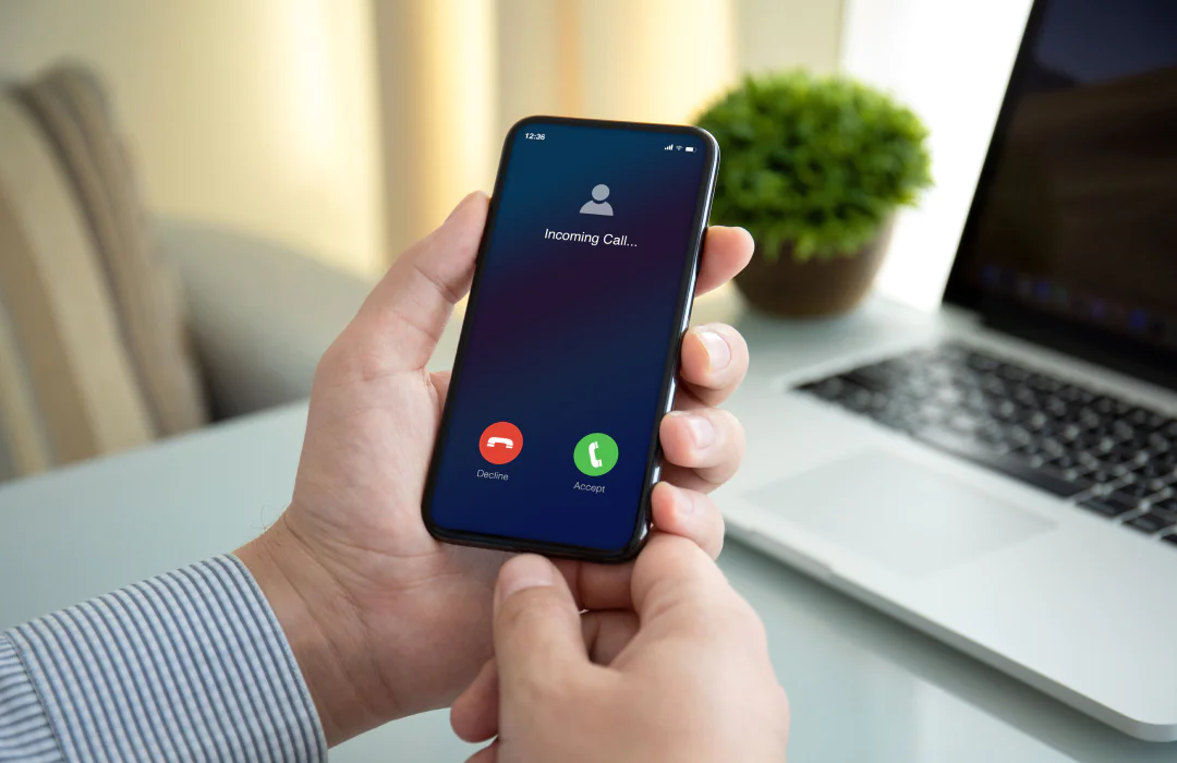 A person holding a smartphone showing an incoming call screen with options to decline or accept