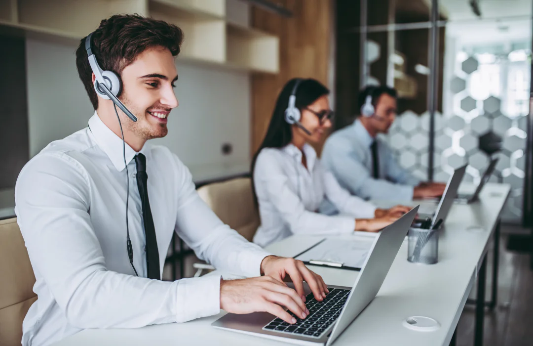 Three customer service representatives at desks wearing headsets and working on laptops.