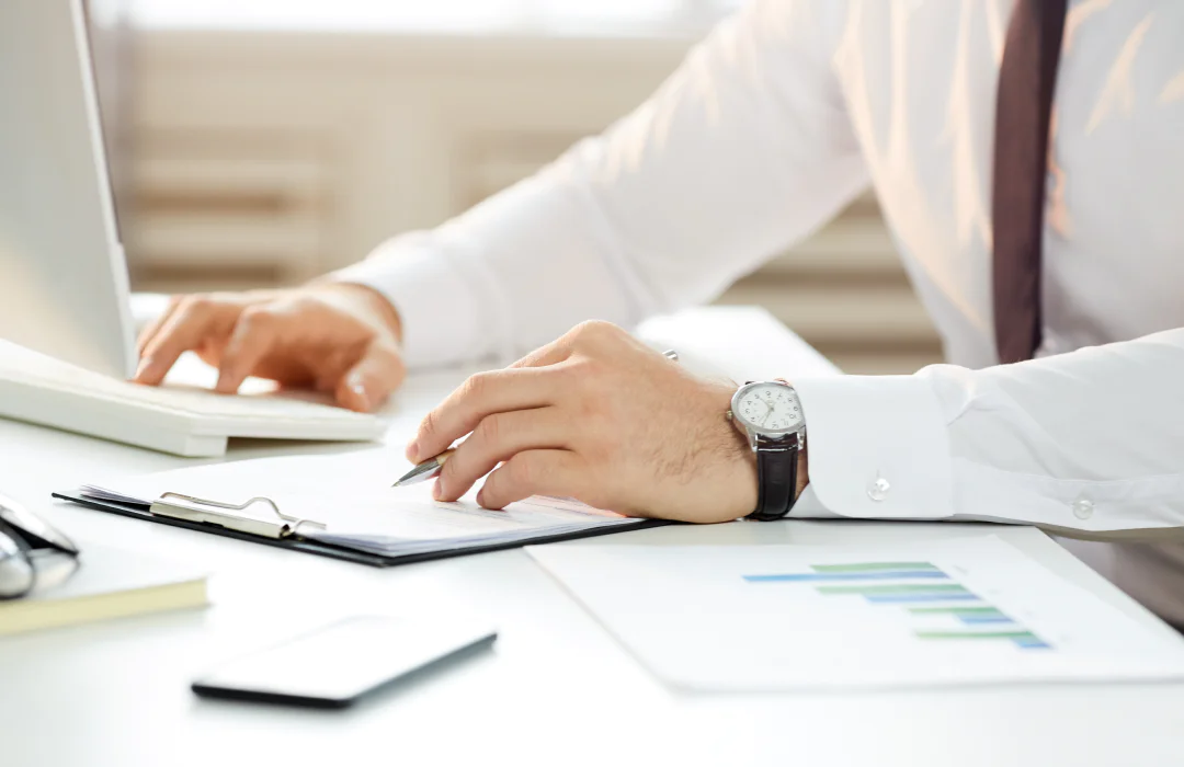 Close-up of a professional reviewing documents with charts and graphs at a desk with a laptop.
