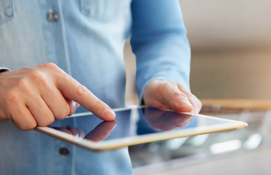 Close-up of a person in a blue shirt using a tablet with one hand.