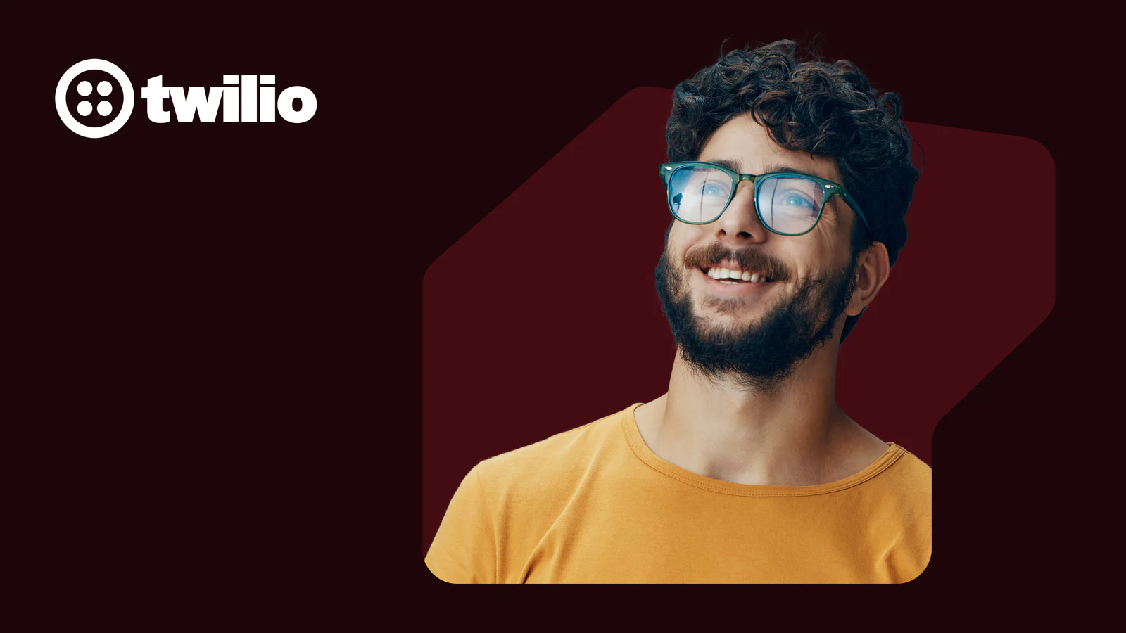 Smiling man wearing glasses and a yellow shirt with Twilio logo on a dark red background.