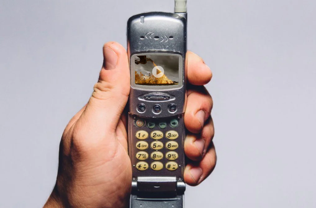 A hand holding an old flip cell phone with a video playing on its screen.