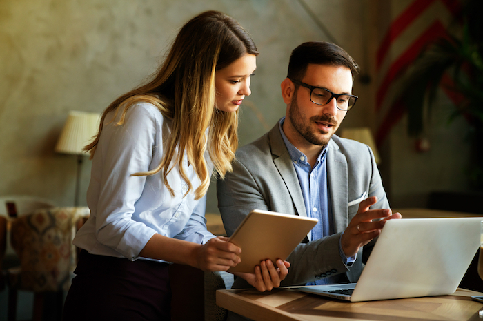 Two colleagues discussing work while looking at a laptop and holding a tablet.