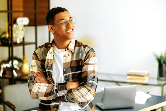 Man in glasses wearing plaid shirt standing with crossed arms in a modern office setting