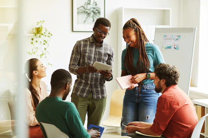 Group of diverse individuals collaborating with tablets and notebooks in an office setting.
