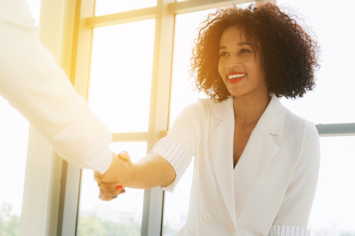 Woman in white suit shaking hands with another person in a bright office.