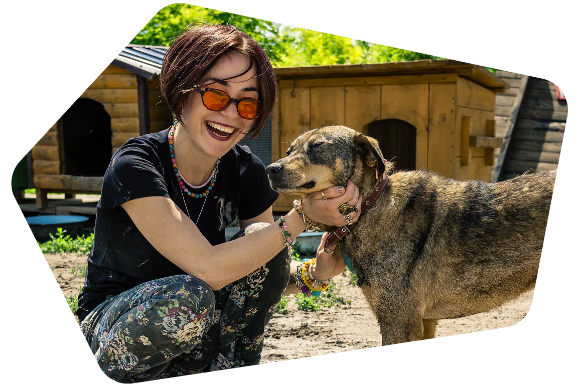 Woman crouches beside a dog, smiling broadly, with dog houses in the background