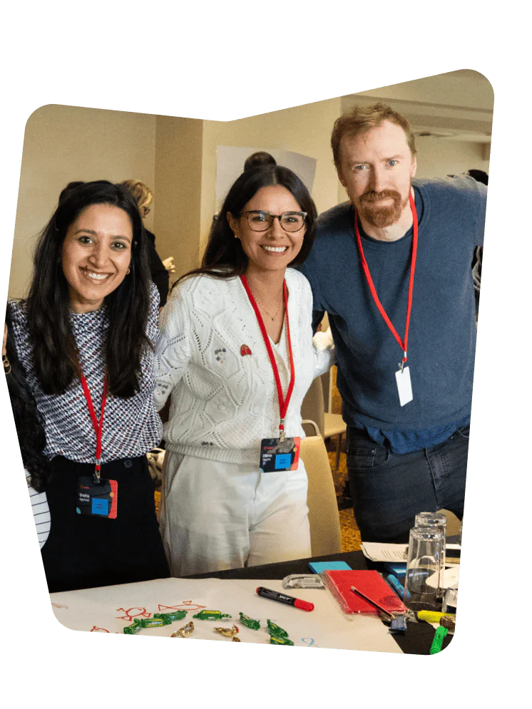 Three people with conference badges, smiling at a table with markers and crafting supplies.