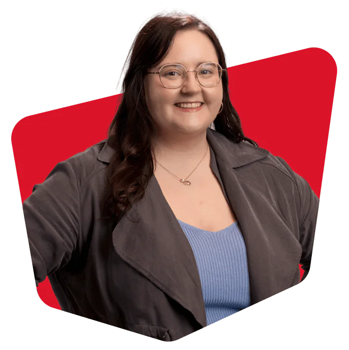 Woman with glasses in gray jacket smiling against a red background