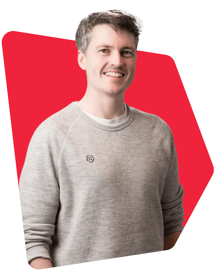Man smiling while wearing a grey sweater in front of a red background