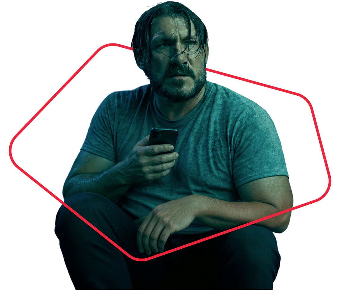 A wet man sitting down and looking concerned while holding a phone in his hand.