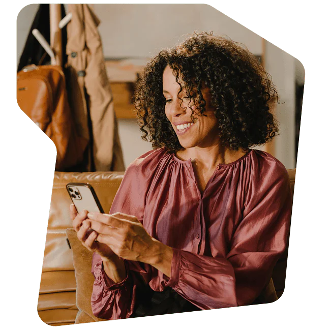 Smiling woman with curly hair sits on a couch, looking at her phone.
