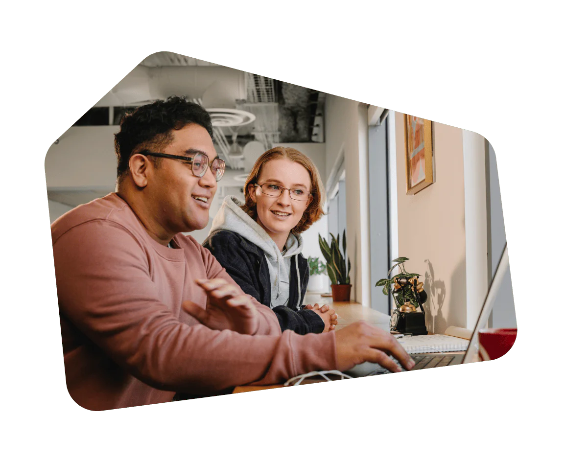 Two colleagues smiling and working together on a laptop in a modern office environment.