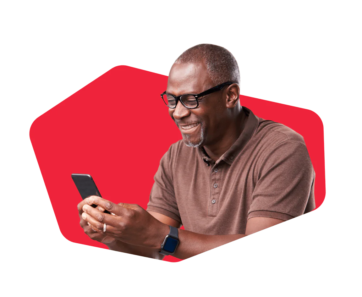 Man Smiling While Looking at His Smartphone Smiling man with glasses using a smartphone against a red background.