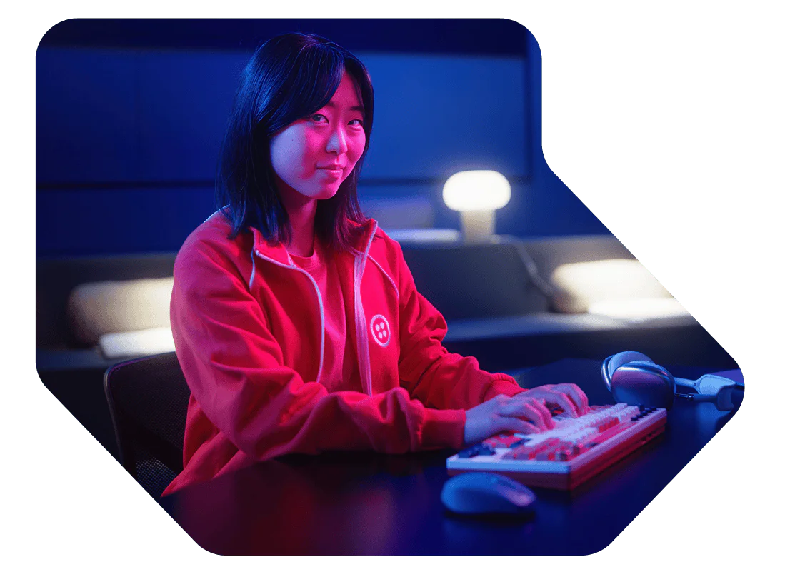 Woman wearing a red jacket typing on a keyboard in a dimly lit room with blue and pink lights