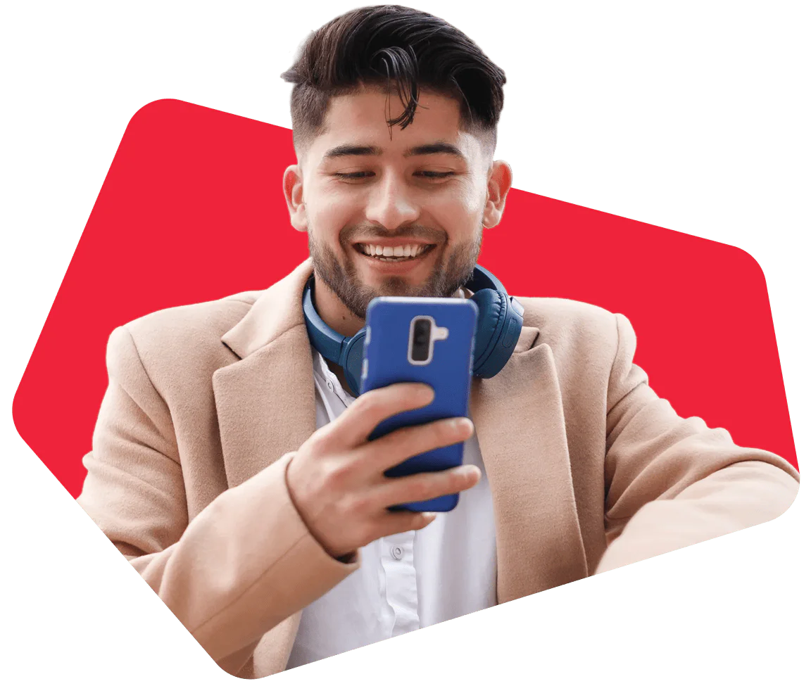 Man with headphones and beige coat smiling at phone with red background