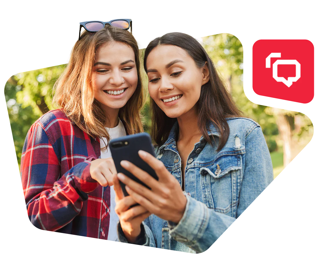Two women outdoors smiling and looking at a smartphone together