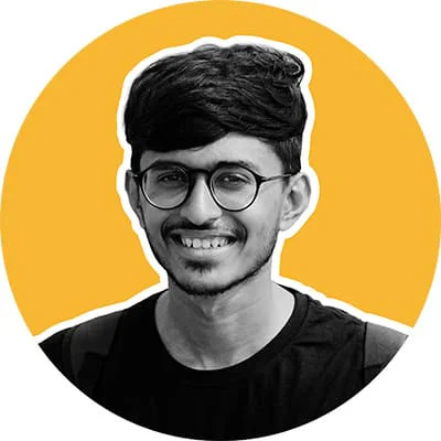 Smiling young man with glasses and dark hair, wearing a black shirt, on an orange background.