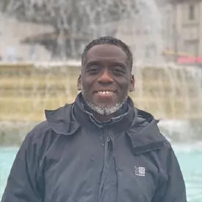 Man in a black jacket smiling while standing in front of a large fountain.