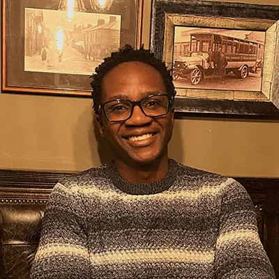 Man with glasses and a sweater smiling in front of vintage framed photos
