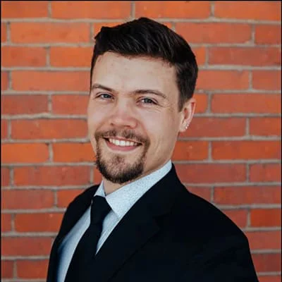 Man in a suit smiling in front of a brick wall