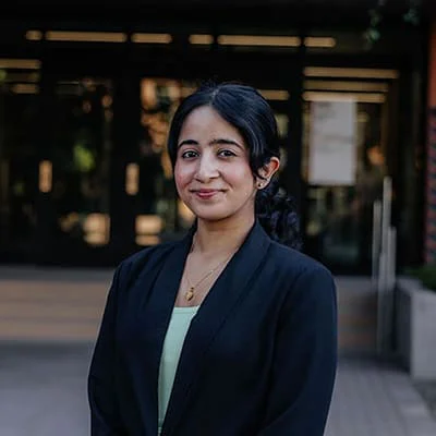 Woman in a dark blazer standing outside a building with a slight smile.