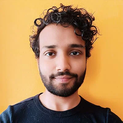 Man with curly hair and beard, wearing a black shirt, standing against an orange background.