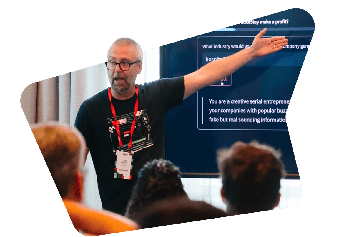 Man in glasses presenting at a seminar with people in the audience.