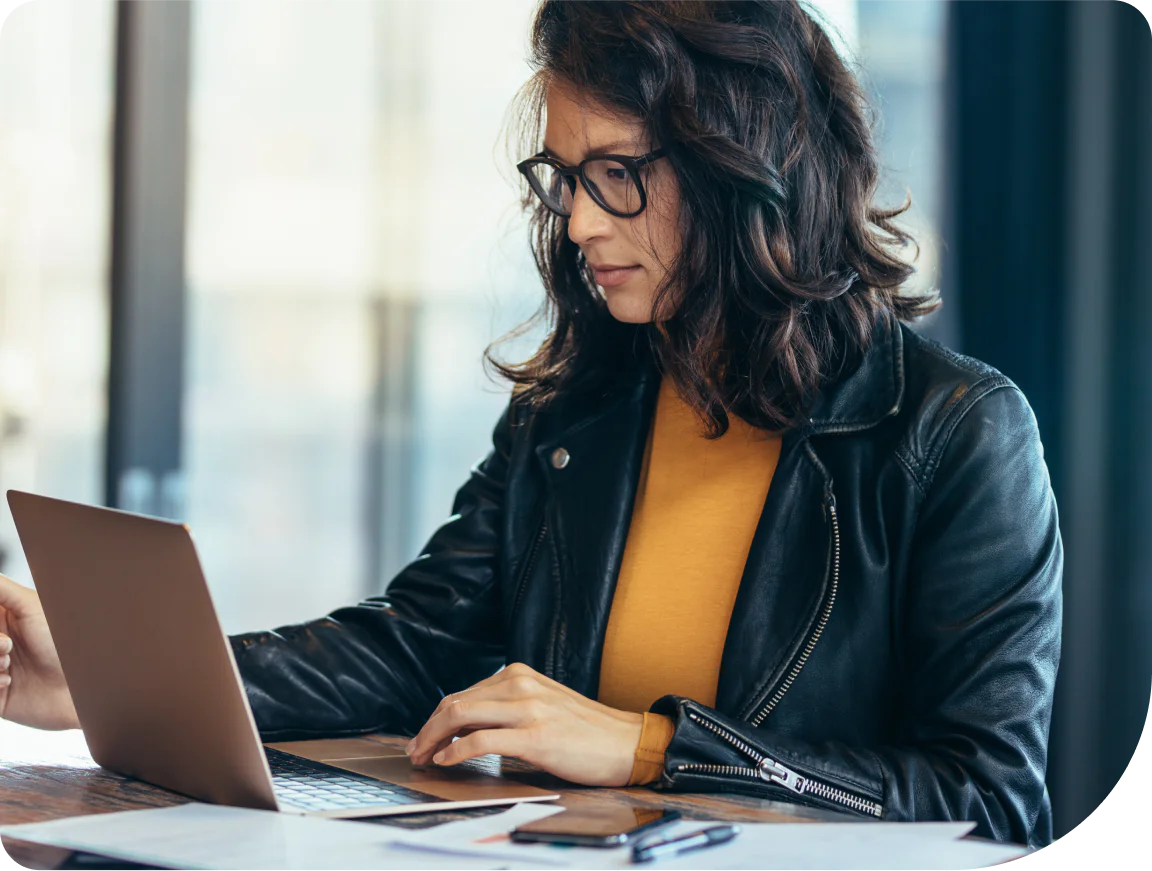 Woman in glasses and a black jacket using a laptop at a desk