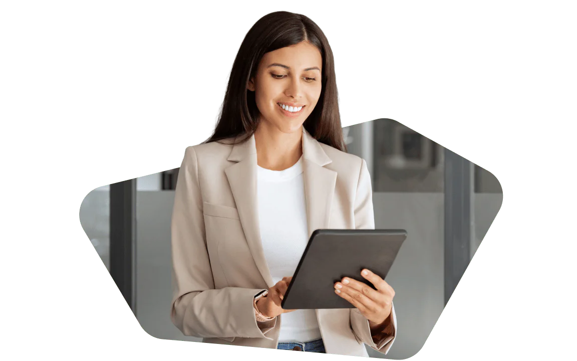 Smiling woman in a beige blazer using a tablet in a modern office environment.