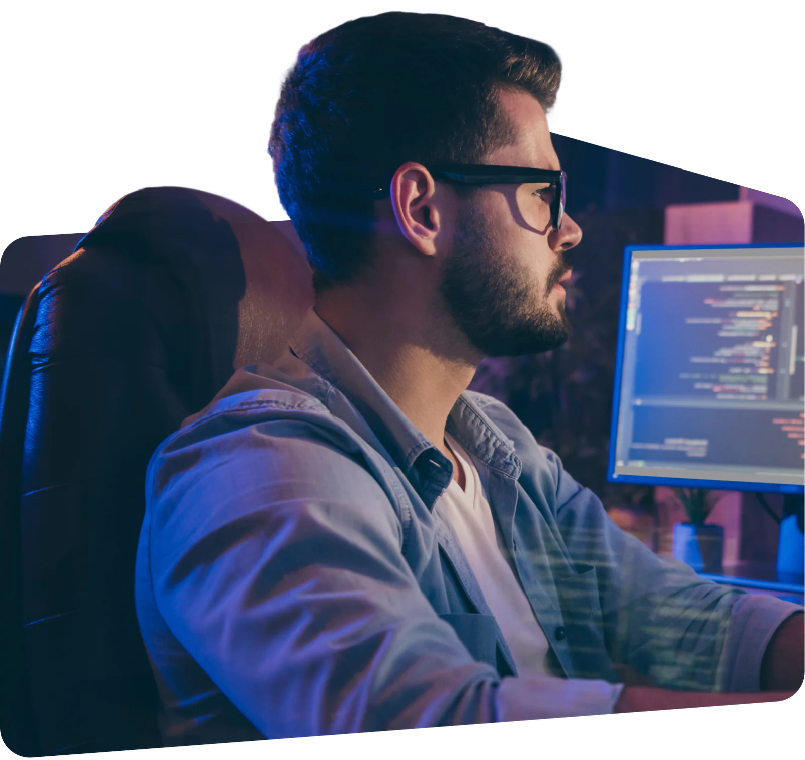 A bearded man wearing glasses, coding on a desktop computer with code visible on the screen.