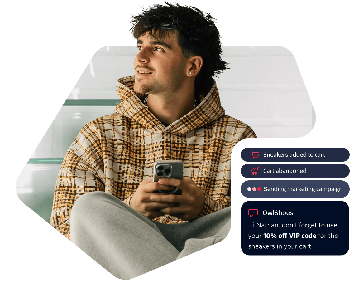 Man in plaid hoodie smiles while holding phone displaying shopping cart notifications.