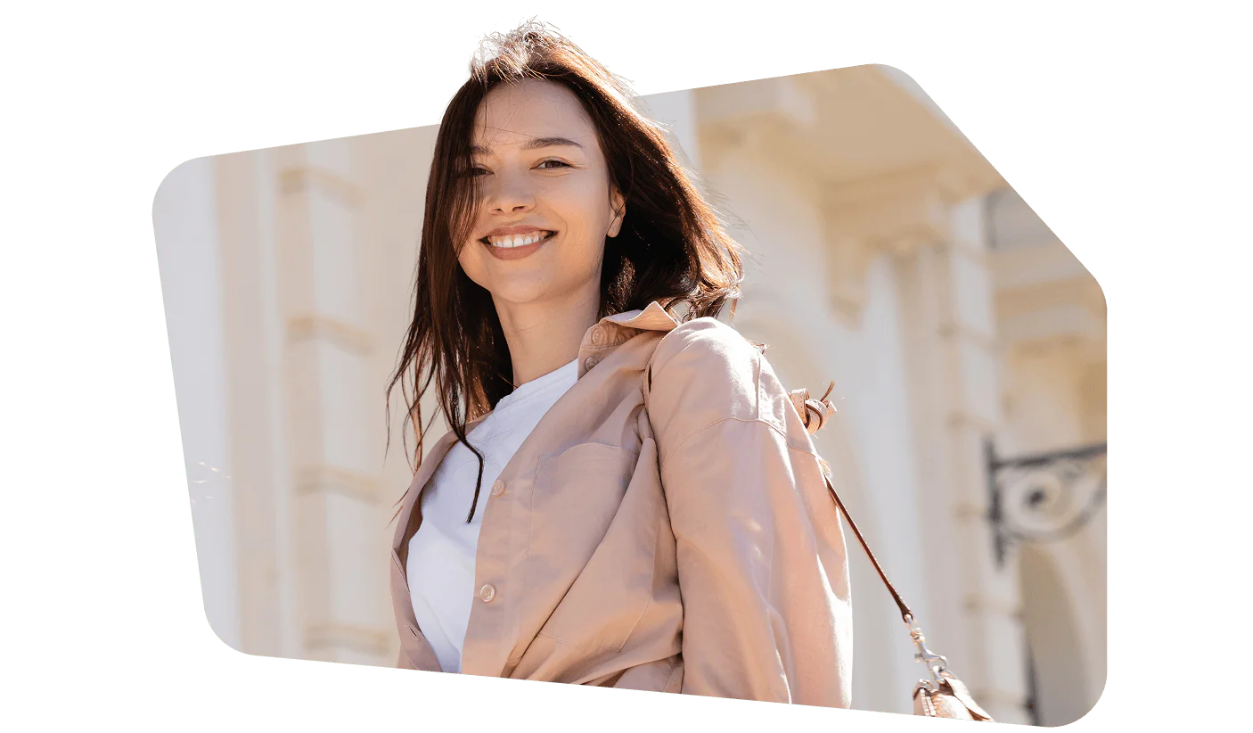 Woman smiling in beige jacket with white top, standing outdoors