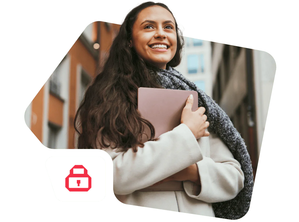 Smiling woman holding a pink tablet while wearing a grey scarf and coat in an urban setting.