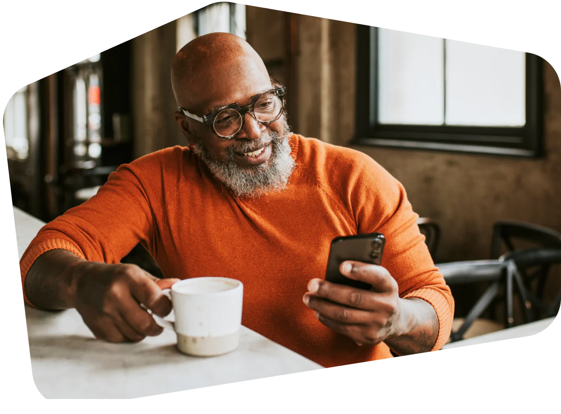 Man enjoying a coffee while browsing his phone at a café. A bald man with glasses smiling at his phone while holding a coffee cup in a café.