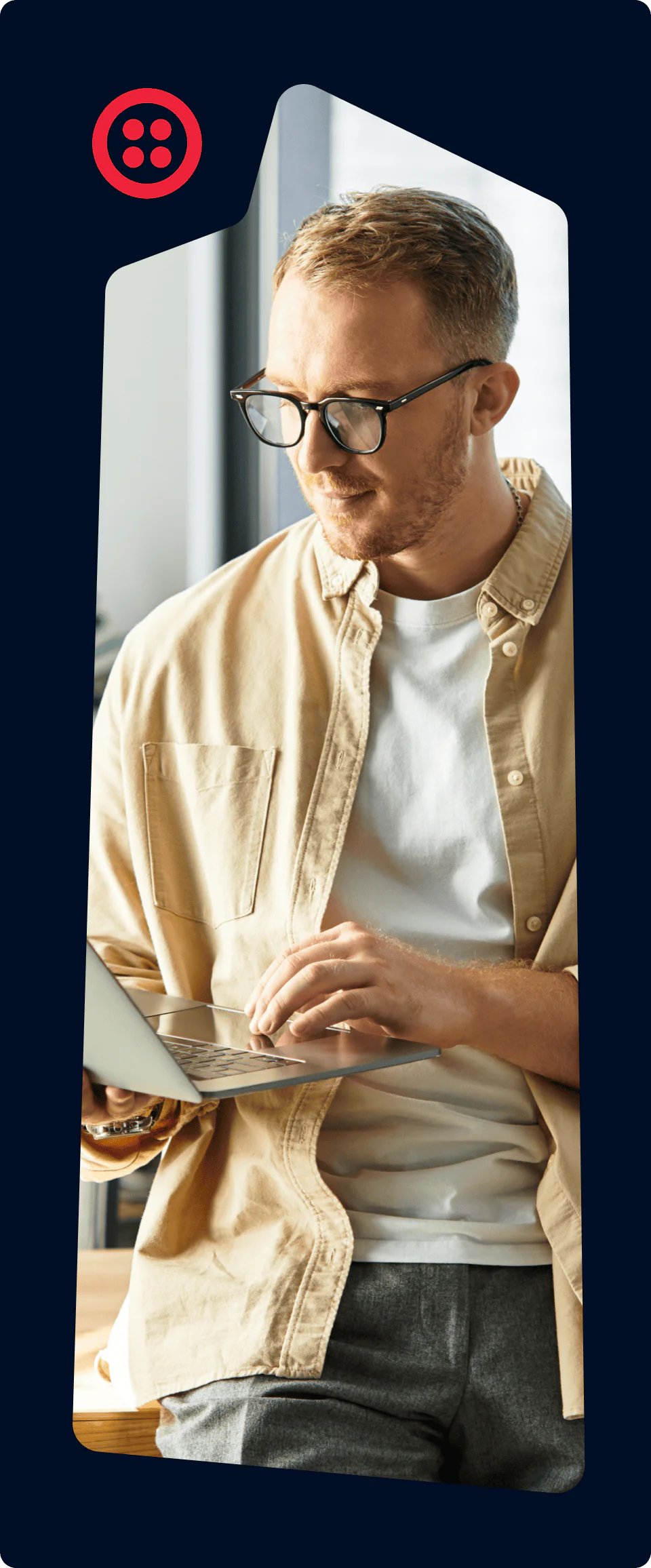 Man wearing glasses and a beige shirt using a laptop in a modern office.