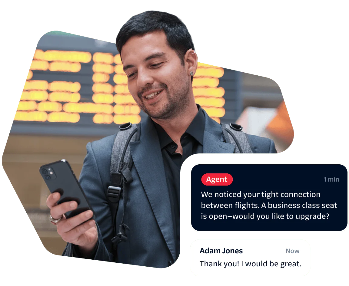 Man checks phone at airport, receives message about upgrading to business class, smiles.